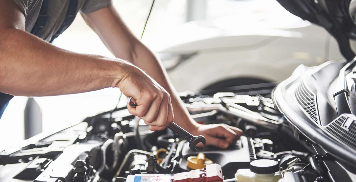 man holding a wrench over an open car bonnet