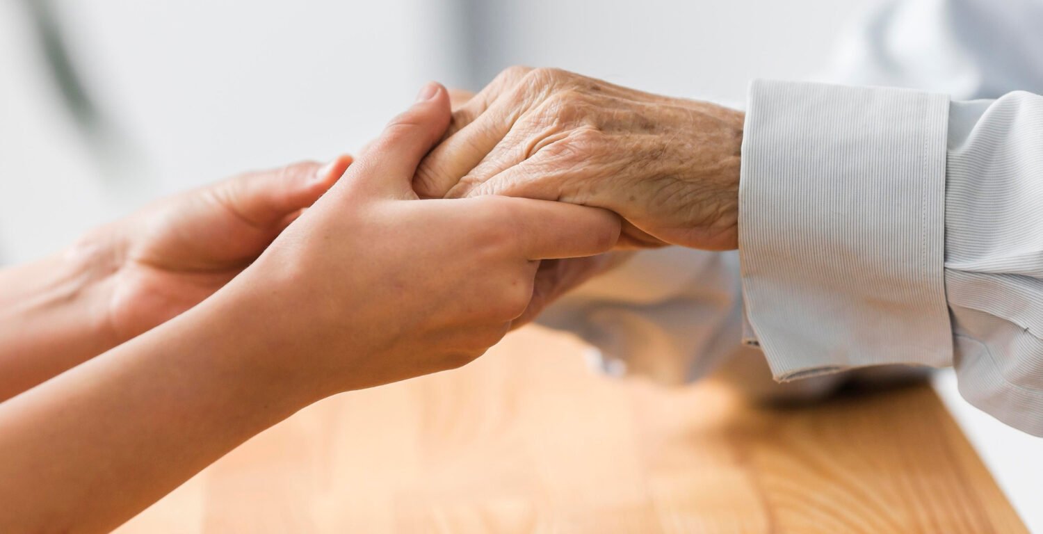 A woman holding an elderly person's hand.