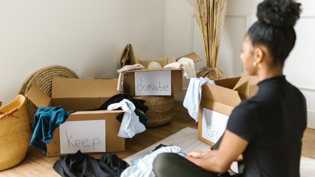 Woman organizing clothes in different boxes labeled as 'Keep' and 'Donate.'
