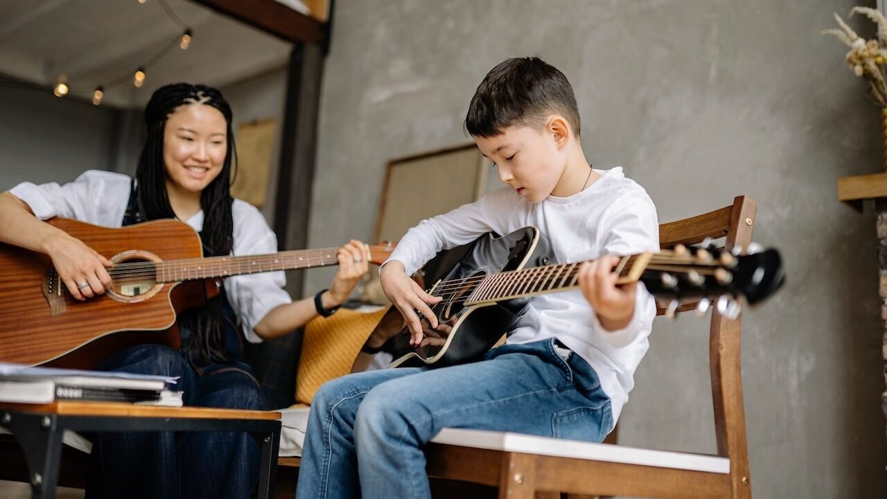 Female music teacher teaching a young boy how to play the guitar. 